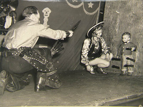 Man in circus throwing knives at boy