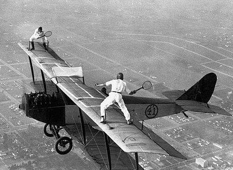 Two men playing tennis on wings of airplane in flight