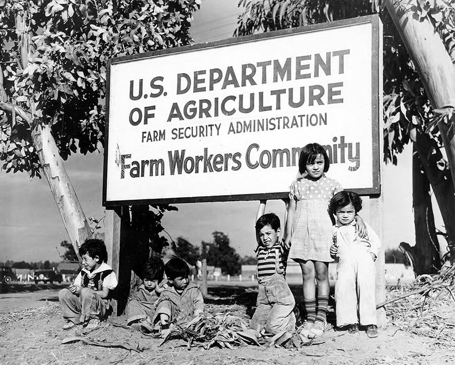 Children under sign that reads: U.S. Department of Agriculture Farm Security Administration Farm Workers Community