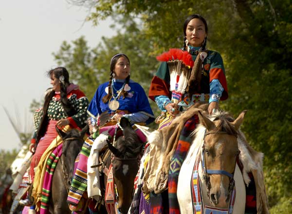 Crow women in dance dresses on horseback