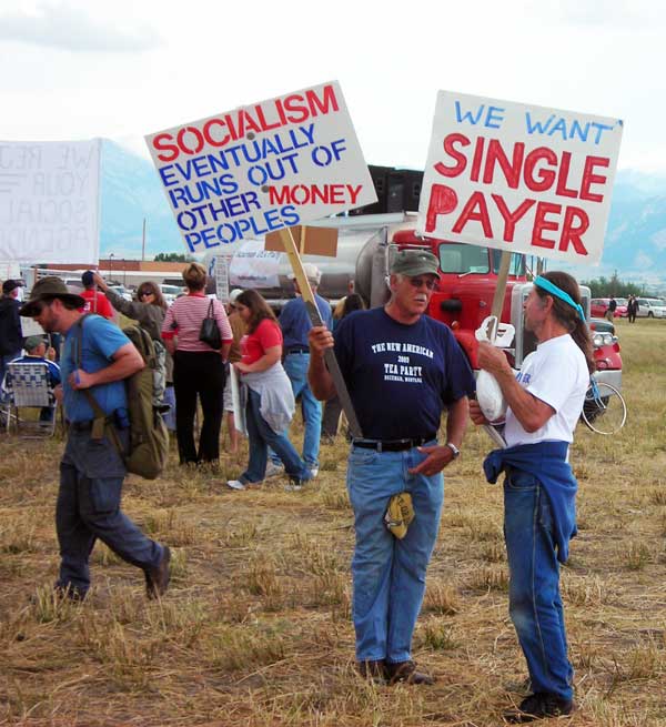 Two men talking, one with anti-socialism sign, the other with single-payer sign
