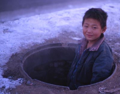 Street kid pops head out of manhole entrance to sewers