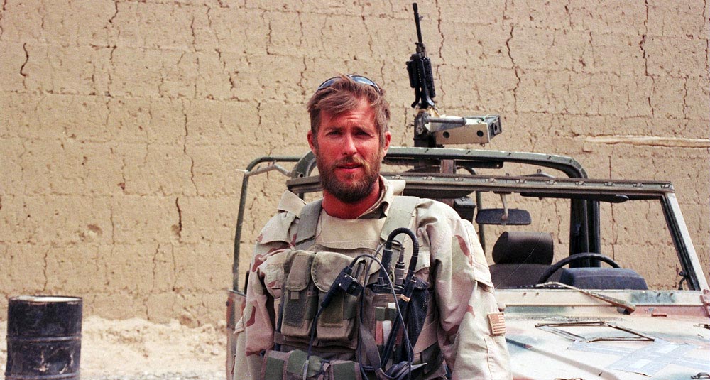 Sgt, Clint Douglas with gear and vehicle in Afghanistan.