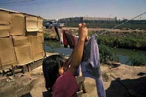 Girl hangs clothes to dry in a squatter's settlement bordering a sewage ditch near a maquiladora industrial park on the Rio Grande.