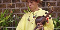 Manop Thammadoonpinij, music teacher and luthier, specializing in traditional Lanna music, playing the Pin Pia, at the street market in Chiang Mai, Thailand.